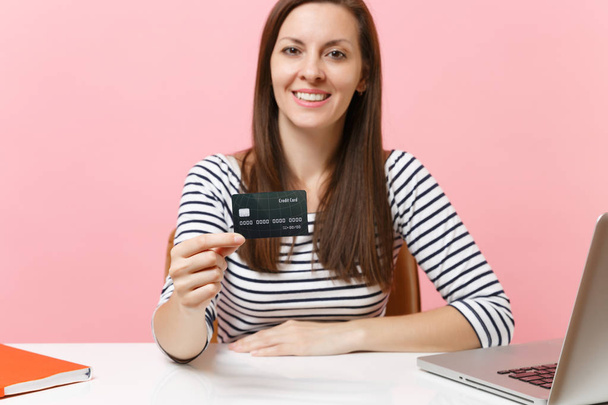 Крупним планом радісна жінка в повсякденному одязі, що тримає роботу по кредитній картці, сидить за білим столом з сучасним ноутбуком ПК ізольовано на пастельно-рожевому тлі. Досягнення концепції бізнес-кар'єри. Копіювати простір
 - Фото, зображення
