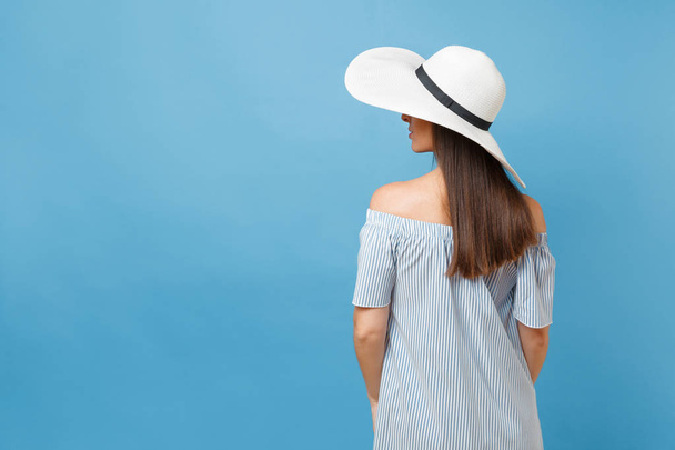 Back view portrait of elegant fashion young woman in white summer large wide brim sun hat, dress put hands on head, looking aside on copy space isolated on blue pastel background. Lifestyle concept - Photo, Image