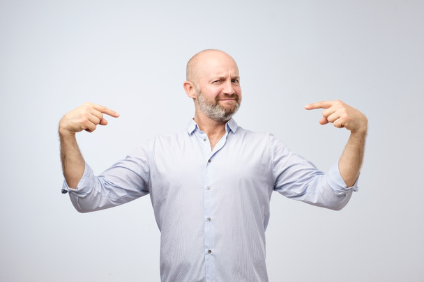 Mature bald adult man with beard standing over grey grunge wall looking confident with smile on face. He is selfish a little and is pointing with fingers at himself - Photo, Image