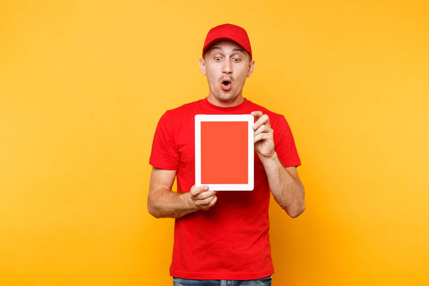 Delivery man isolated on yellow orange background. Professional male employee courier in red cap, t-shirt holding tablet computer with blank empty screen. Service concept. Copy space. Mockup template - Fotó, kép