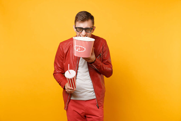 Portrait vogue young man in 3d glasses, leather jacket, t-shirt watching movie film, holding popcorn, cup of soda isolated on bright yellow background. People sincere emotions lifestyle concept. - Photo, image