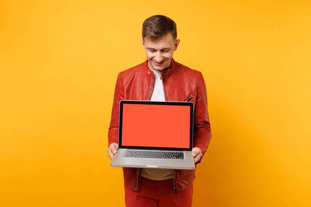 Portret vogue leuke jongeman in rode lederen jas, t-shirt houden laptop computer leeg leeg scherm geïsoleerd op heldere gele achtergrond. Mensen oprechte emoties levensstijl concept. Gebied van de reclame - Foto, afbeelding