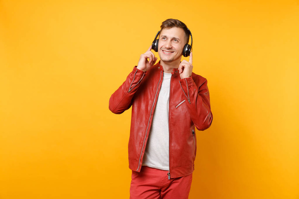 Portret vogue szczęśliwy zabawa młodego człowieka w czerwona skórzana kurtka, t-shirt słuchać muzyki w słuchawkach na białym tle na jasne najpopularniejsze żółte tło. Koncepcja życia szczere emocje ludzi. Powierzchnia reklamowa - Zdjęcie, obraz