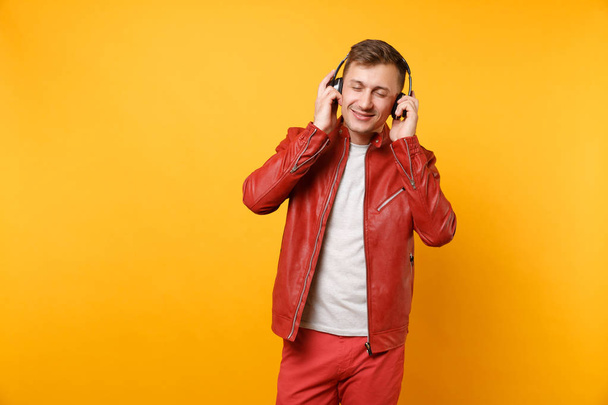 Retrato moda feliz divertido jovem em jaqueta de couro vermelho, t-shirt ouvir música em fones de ouvido isolados no fundo amarelo tendência brilhante. Conceito de estilo de vida de emoções sinceras. Área publicitária
 - Foto, Imagem