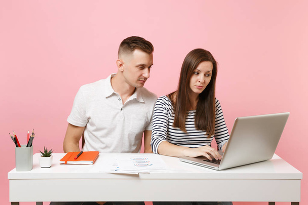 İki genç yoğun iş kadın erkek arkadaşları iş pastel pembe arka plan üzerinde izole çağdaş dizüstü bilgisayar ile beyaz masa başında oturmak. Başarı kariyer kavramı. Alan reklam, kopyalama co çalışma - Fotoğraf, Görsel
