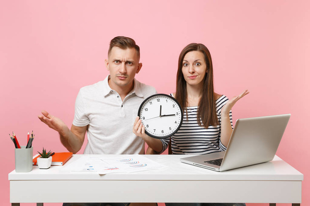 Two young fun shocked business woman man colleagues sit work at white desk with clock, laptop isolated on pastel pink background. Achievement career concept. Copy space advertising, youth co working - Photo, Image