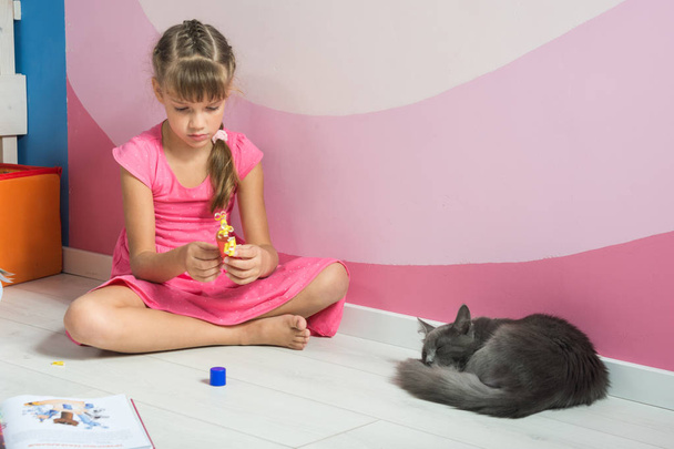 A girl is making figures out of colored paper, a domestic cat is sleeping nearby - Photo, Image