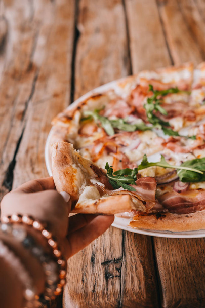 Ženská ruka ukousnout kus pizza carbonara na rustikální dřevěný stůl. Potraviny fotografie konceptu. Pohled shora - Fotografie, Obrázek