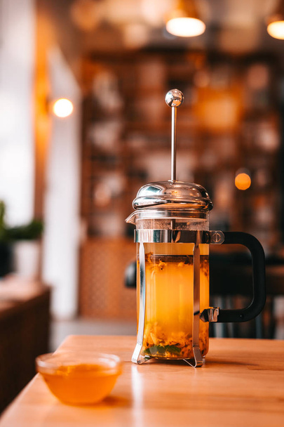 Чай из облепихи в французском прессе с медом на деревянном столе в кафе
.  - Фото, изображение