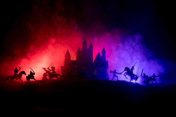 Medieval battle scene with cavalry and infantry. Silhouettes of figures as separate objects, fight between warriors on dark toned foggy background with medieval castle. Selective focus - Photo, Image