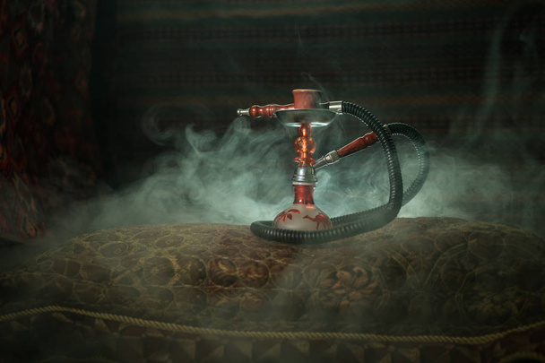 Hookah carbones calientes en el tazón de shisha haciendo nubes de vapor en el interior de Arabia. Adorno oriental en la alfombra. Elegante shisha oriental con luz de fondo. Para el anuncio de Shisha. Enfoque selectivo
 - Foto, Imagen