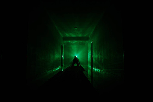 Ανατριχιαστικό σιλουέτα στο σκοτεινό εγκαταλελειμμένο κτίριο. Τρόμου σχετικά με μανιακός έννοια ή σκοτεινός διάδρομος με πόρτες γραφείων και φώτα με σιλουέτα του τρόμου τρομακτικό πρόσωπο που στέκεται με διαφορετικές πόζες. - Φωτογραφία, εικόνα