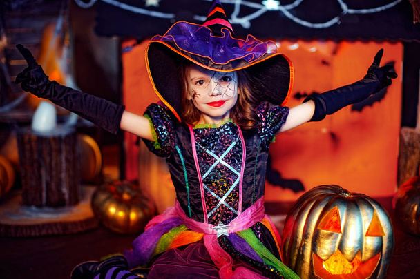 Happy Halloween. A little beautiful girl in a witch costume celebrates with pumpkins - 写真・画像