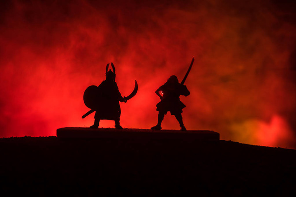 Silhouette zweier mittelalterlicher Krieger im Duell. Bild mit zwei Kämpfern mit Schwert vor dunkel getöntem Nebelhintergrund. Selektiver Fokus. - Foto, Bild