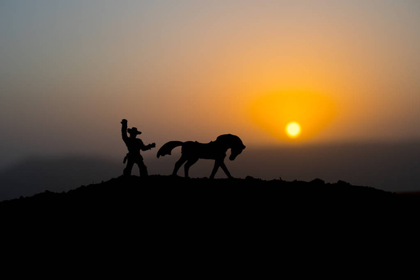 カウボーイのコンセプトです。日没時の馬とカウボーイのシルエット。黄色の空と山の上のカウボーイのシルエット。選択と集中 - 写真・画像