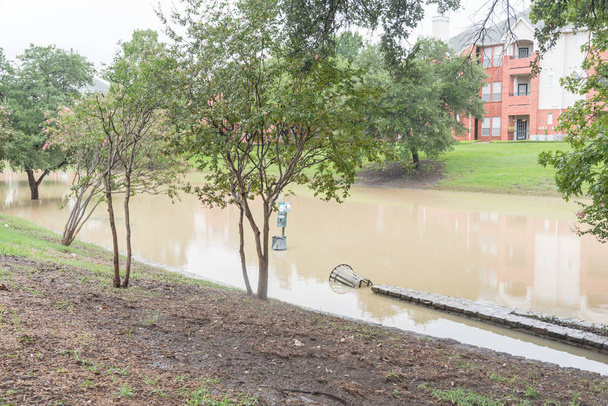 Zaplavený u řeky cesta poblíž nábřežní apartmánový komplex v příměstské Dallas Fort Worth, Texas, Usa. Zaplavena pes odpadní stanice a venkovní ocelové smetí nádoby - Fotografie, Obrázek