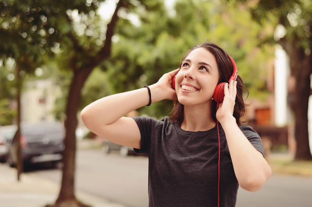 Portrait of young beautiful woman with red headphones listening music. Outdoors. Urban concept. - Фото, зображення