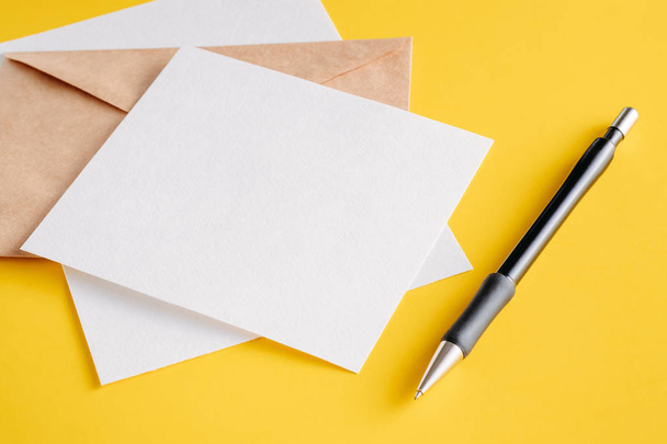 White paper empty sheets cards, kraft envelope and pen on a yellow background. Mockup for design - Foto, Imagen