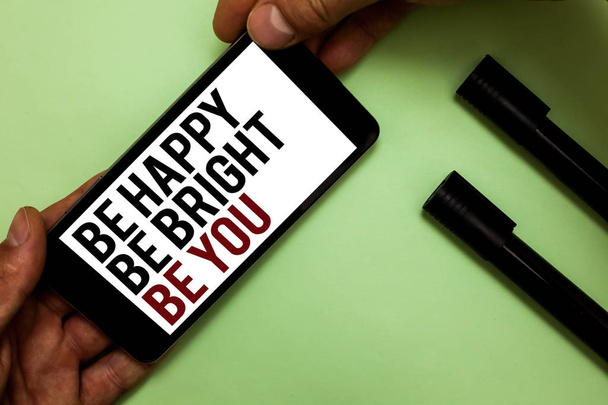 Text sign showing Be Happy Be Bright Be You. Conceptual photo Self-confidence good attitude enjoy cheerful Mans hand hold iPhone with black and red words near two black marker. - Photo, Image
