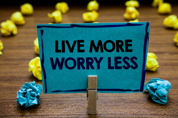 Написання тексту Live More Worry Less. Концепція означає Мати добру мотивацію бути недбалим насолоджуватися життям Розмита дерев'яна палуба жовтий і синій лоб на сторінці руків'я затискача на папері з текстом
. - Фото, зображення