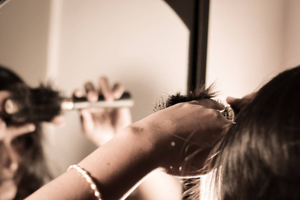 Κυρία χτενίζει τα μαλλιά της με βούρτσα στο καθρέφτη. - Φωτογραφία, εικόνα