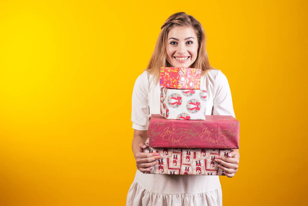 Portrait of a happy smiling girl in dress holding present boxes isolated over yellow background. - Photo, Image