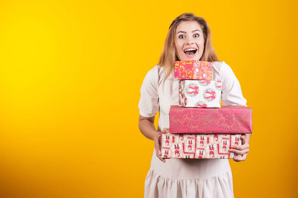 Портрет щасливої дівчини з відкритим ротом в сукні, що тримає подарункові коробки ізольовані на жовтому тлі
. - Фото, зображення