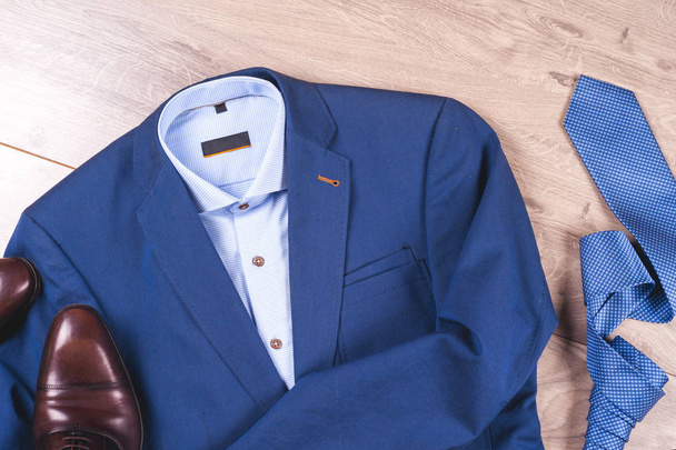 набор классической мужской одежды - синий костюм, рубашки, коричневые туфли, пояс и галстук на деревянном фоне. - Фото, изображение