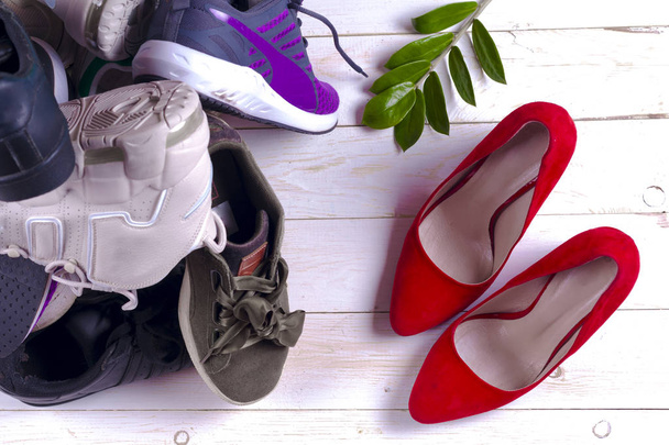 Μεγάλο σωρό από διαφορετικά αθλητικά παπούτσια και τα κόκκινα ψηλοτάκουνα Γυναικεία παπούτσια σε λευκό φόντο. - Φωτογραφία, εικόνα