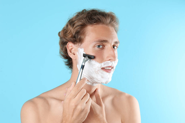 Handsome young man shaving on color background - Фото, изображение
