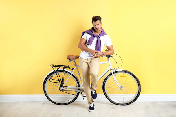 Handsome young hipster man with bicycle near yellow wall - Φωτογραφία, εικόνα