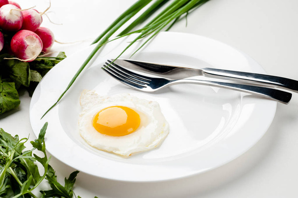 Scrambled eggs on a white plate with a fork and a knife. Green onion near the plate. - Photo, Image