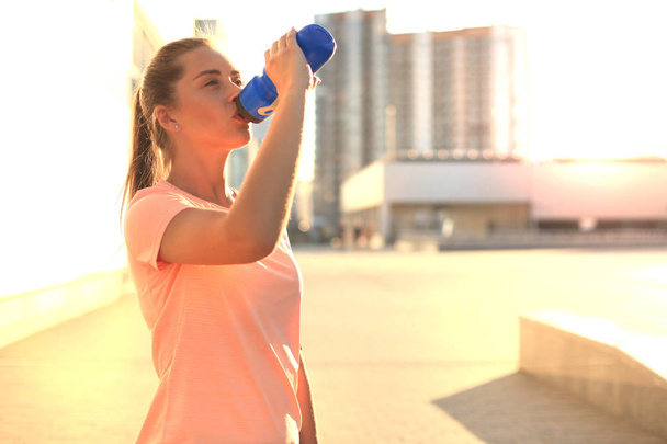 Young female runner is having break, drinking water during the run in city center. - Photo, Image