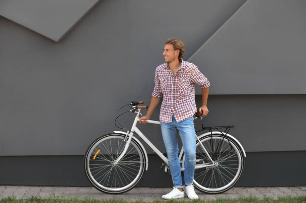 Bonito jovem com bicicleta perto de parede cinza ao ar livre
 - Foto, Imagem