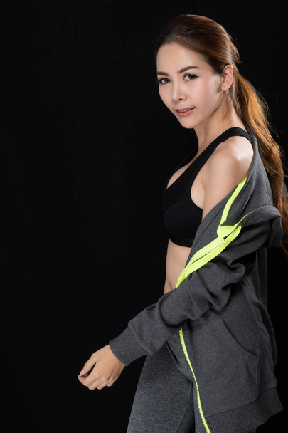 Asiática chica (Edad 20-30 años) en un traje de entrenamiento gris sobre un fondo negro
. - Foto, Imagen
