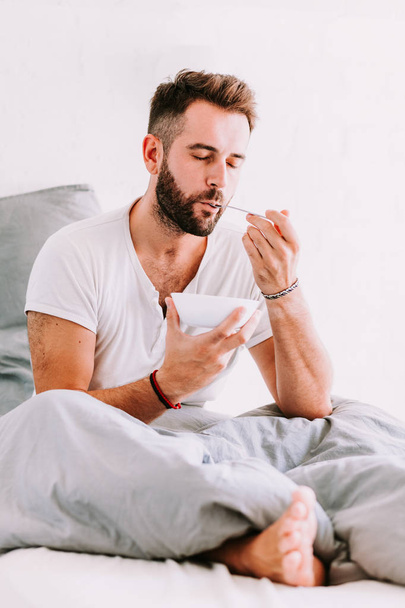 Νεαρός άνδρας τρώει πρωινό στο κρεβάτι - Φωτογραφία, εικόνα