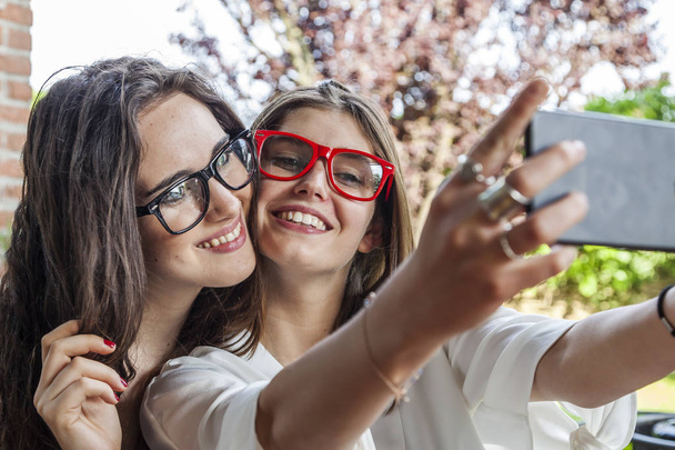 two female young friends take a selfie hugged together outdoors with funny faces - Foto, Imagen