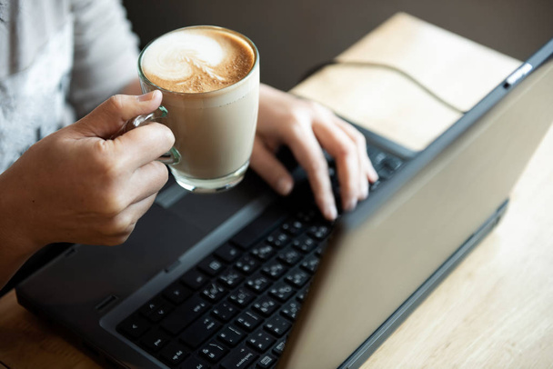 Coffee in hand office girl.She is using laptop. - Zdjęcie, obraz