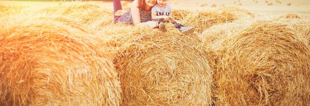Mãe e filho ao pôr-do-sol sentam-se num campo num palheiro e abraçam-se contra o pôr-do-sol. Vida rural, um passeio na natureza, umas férias no campo
 - Foto, Imagem