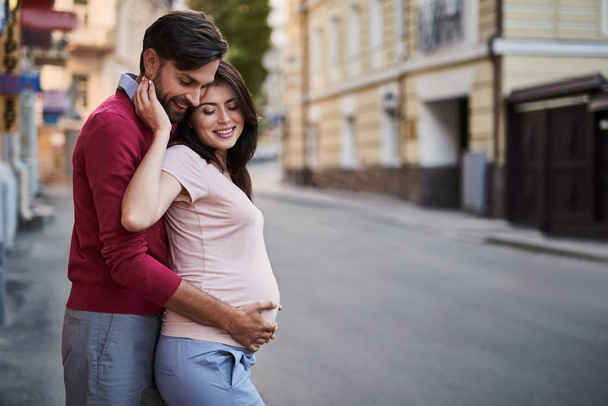 Smiling bearded man holding belly of his lovely pregnant wife - Photo, Image