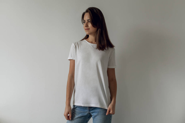 Young hipster smiling girl wearing blank white t-shirt and blue jeans, mock-up of blank white t-shirt, white background - Foto, immagini