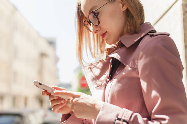 Happy smiling businesswoman using modern smartphone device, successful female entrepreneur using cellphone wireless connection walking along the street, young woman browsing mobile phone outside - 写真・画像