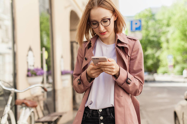 Happy smiling businesswoman using modern smartphone device, successful female entrepreneur using cellphone wireless connection walking along the street, young woman browsing mobile phone outside - Photo, image