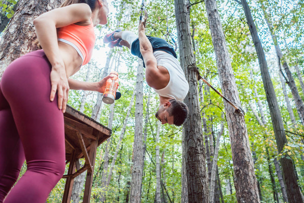 Woman and man doing athletic training in the woods at rings - 写真・画像