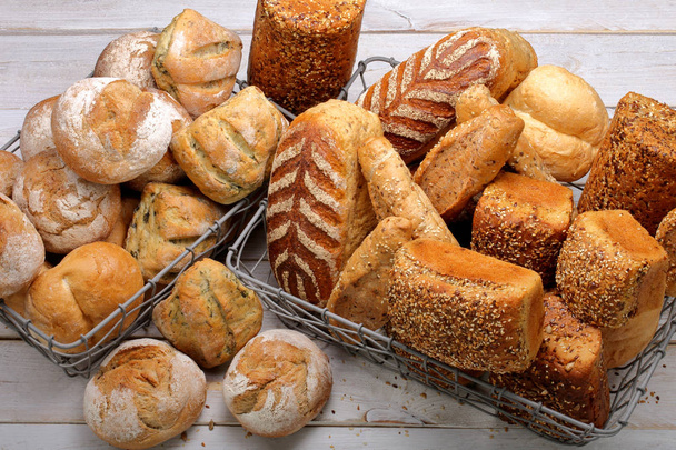 Diferentes tipos de pão e pães em uma cesta de metal em um fundo de madeira
 - Foto, Imagem
