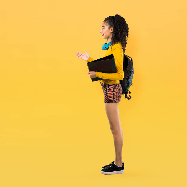 Teljes test tizenéves diák lány göndör haja kezet egy jó üzlet lezárásának a sárga háttér - Fotó, kép