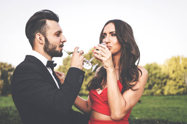 Ευτυχισμένο ζευγάρι των εραστών με ένα ποτήρι κρασί ή σαμπάνια στέκεται σε εξωτερικούς χώρους. - Φωτογραφία, εικόνα