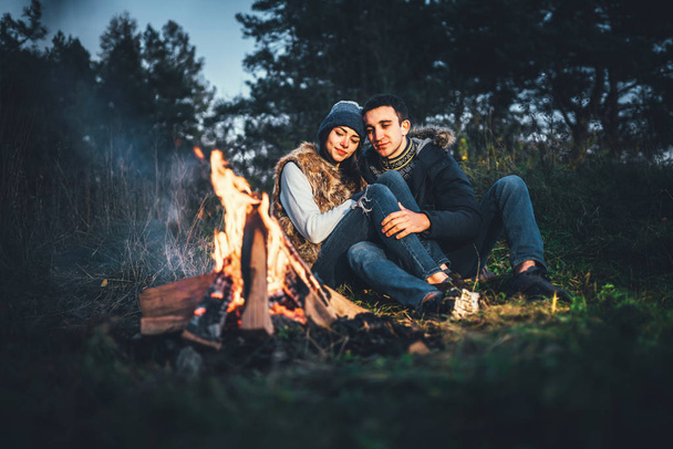 Pretty young couple relaxing near bonfire in the forest at evening time - Fotografie, Obrázek
