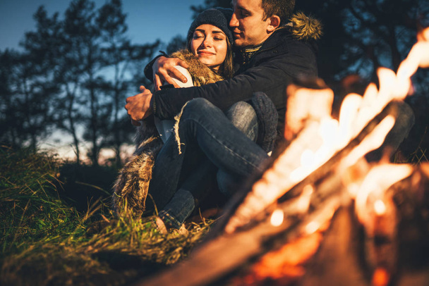Pretty young couple relaxing near bonfire in the forest at evening time - Fotografie, Obrázek