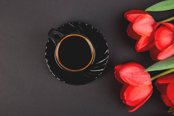Ramo de tulipanes rojos y taza de café sobre fondo negro. Acostado. Día de la Madre o la Mujer. Tarjeta de felicitación. Buenos días, desayuno. Copiar espacio. Primavera
. - Foto, imagen